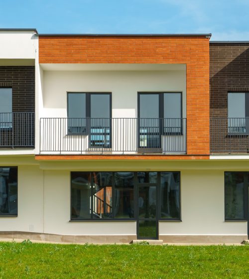 The exterior of a modern townhouse. The concept of building multi-family residential townhouses. For sale or rent a cozy small house with a beautiful green lawn.